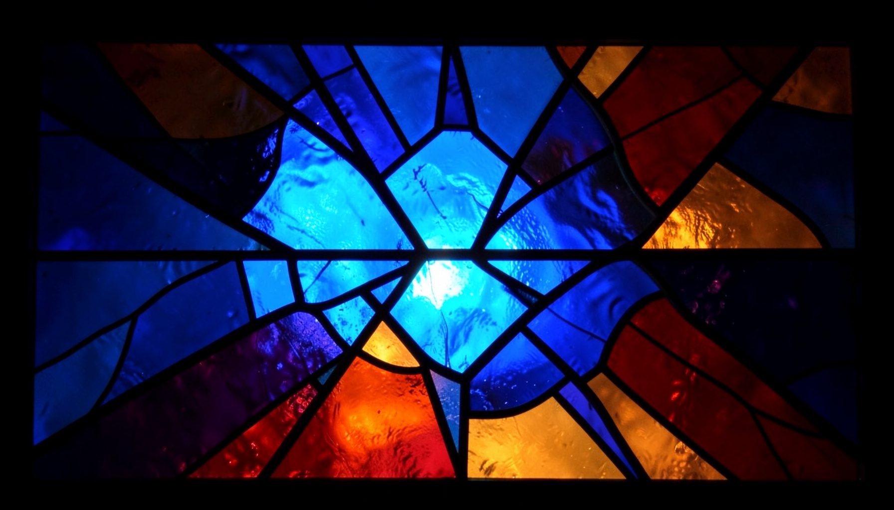 A stained-glass composition with bold leaded segments in deep indigo, amber, and ruby tones, radiating warm light through geometric panels